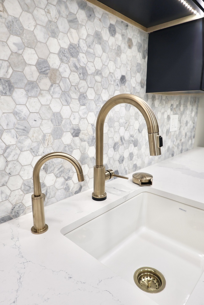 Gold kitchen faucet detail over quartz countertop with hex tile backsplash by Clear Contractors in Crown Point, IN