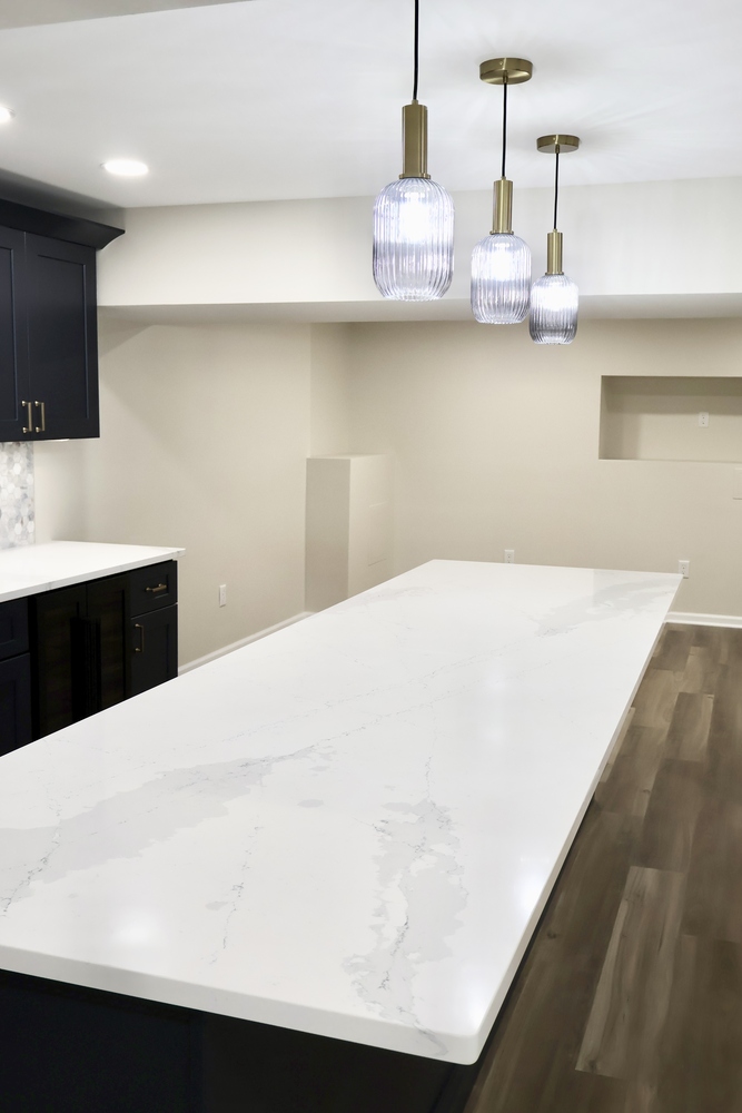Large kitchen island with soft veining and overhead lighting in Crown Point, IN basement by Clear Contractors