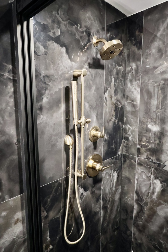 Brushed gold shower fixtures mounted on dark marble tile in a custom home by Clear Contractors in Crown Point, IN.