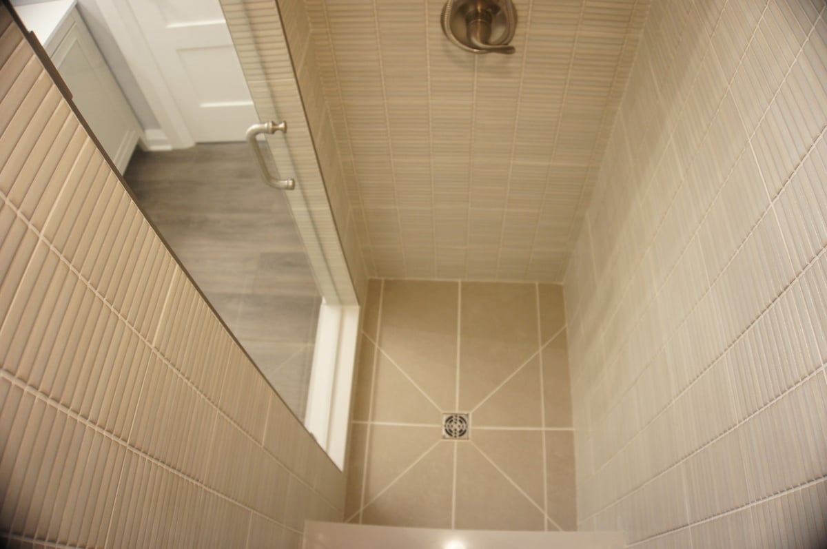 Beige tile shower floor and glass enclosure for Basement + Bathroom Remodel in St. John