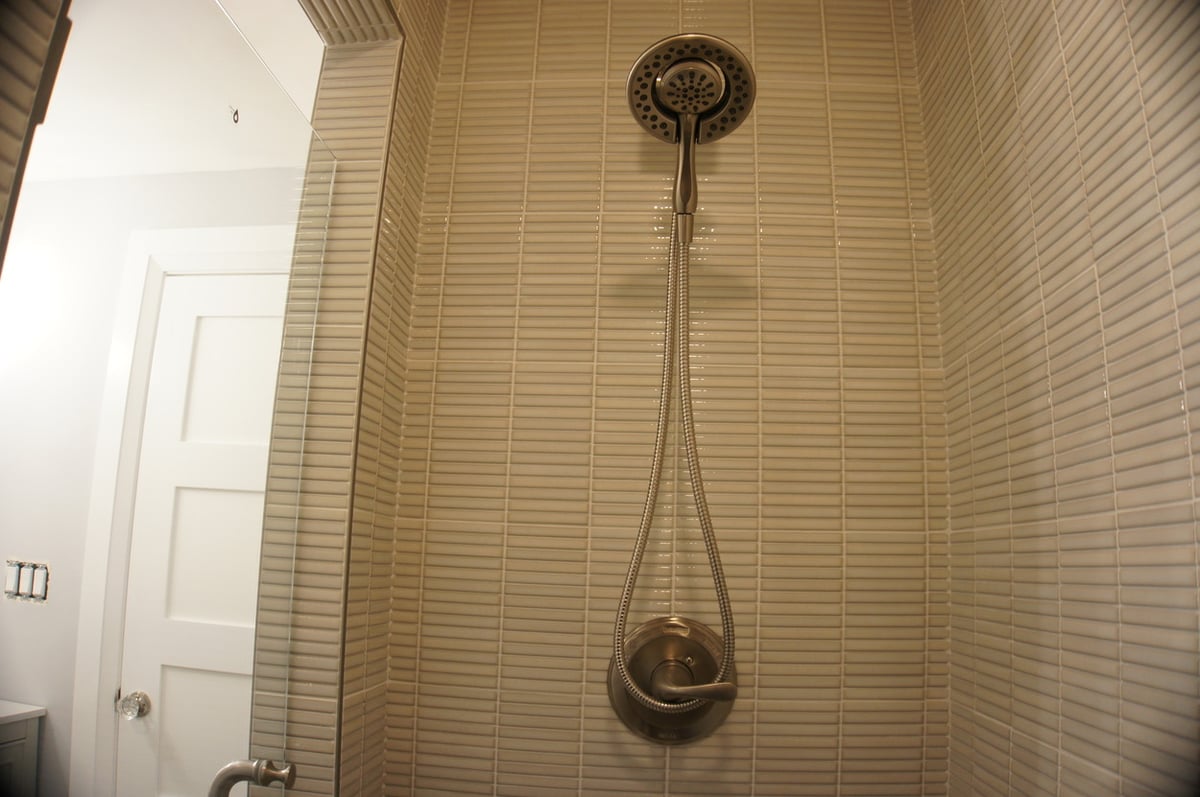 Beige tiled shower with detachable chrome showerhead for Basement + Bathroom Remodel in St. John