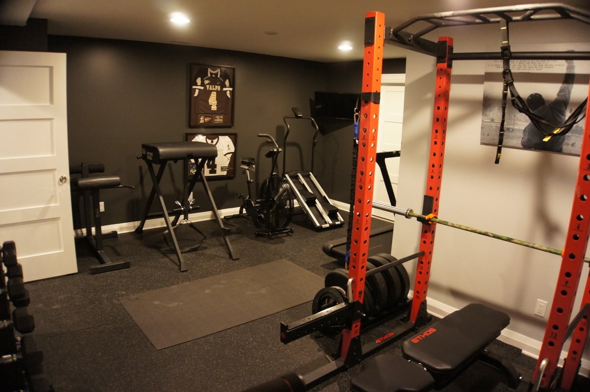 Home gym with red squat rack and cardio machines for Basement + Bathroom Remodel in St. John