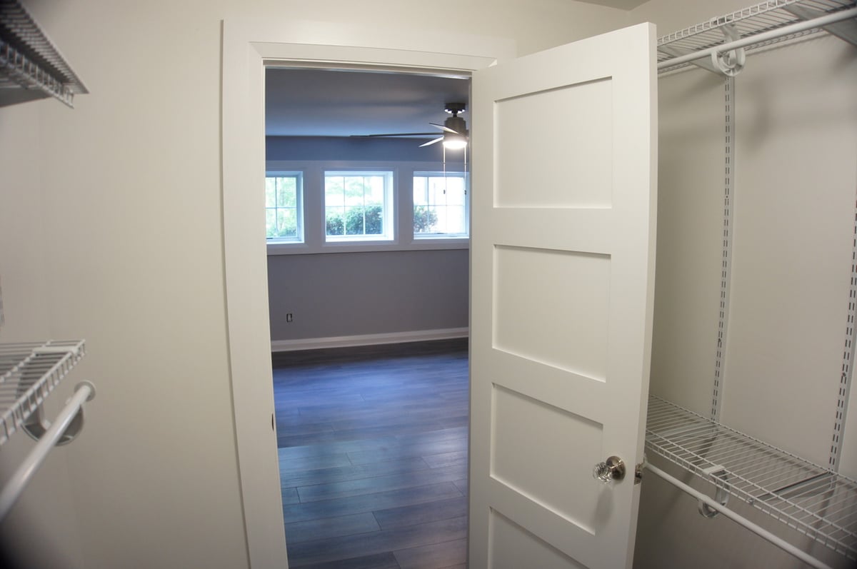 Walk-in closet with white shelving and view into finished basement room for Basement + Bathroom Remodel in St. John