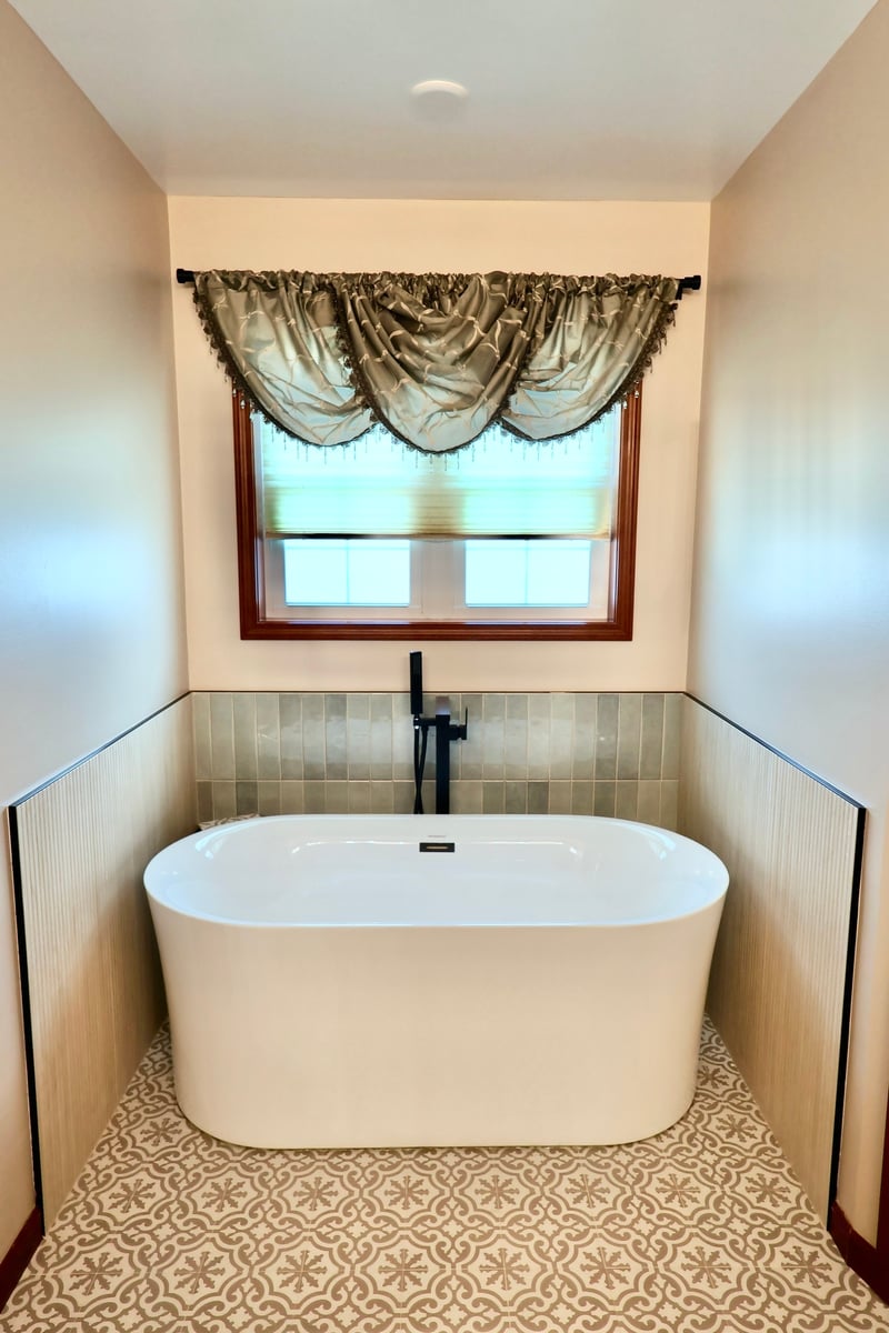 Freestanding soaking tub with black fixtures and patterned floor in Lowell bathroom remodel