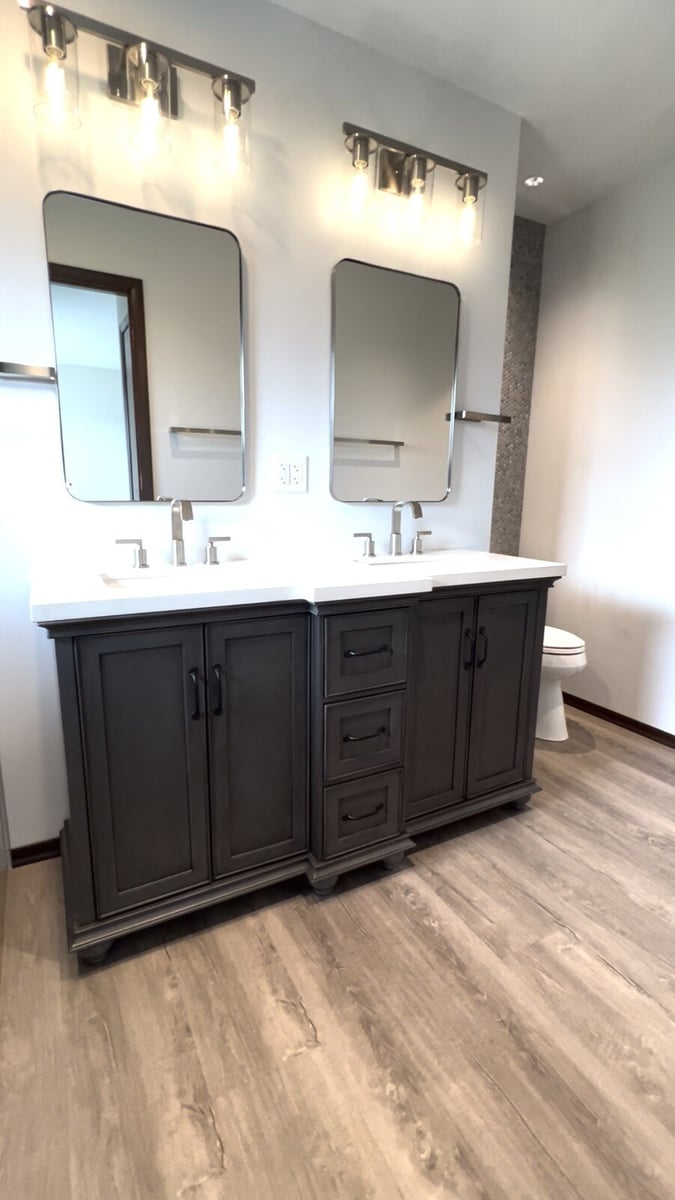 Contemporary dual sink vanity with a white countertop and modern lighting fixtures, remodeled by Clear Contractors in Northwest Indiana