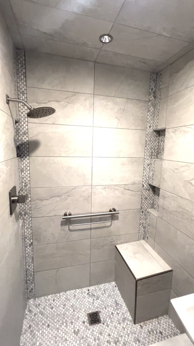 Walk-in shower with gray tile walls and mosaic pebble flooring, remodeled by Clear Contractors in Northwest Indiana